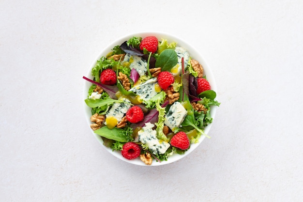 Salad with lettuce roquefort cheese raspberries walnuts and vinaigrette on white background