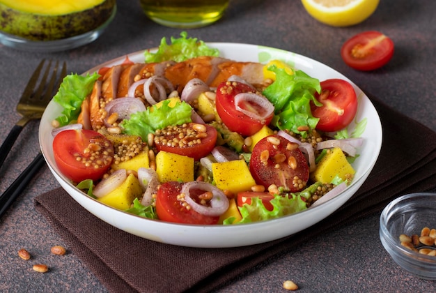 Salad with mango smoked chicken and cherry tomatoes served with green lettuce leaves in a plate on a brown background