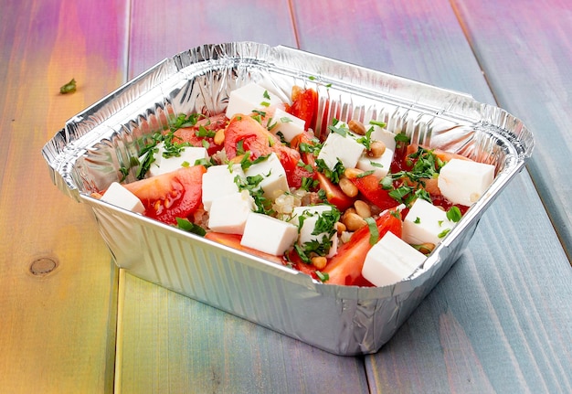 Salad with mozzarella pine nuts and cherry tomatoes in containers on a colored background Takeaway Diet and healthy food