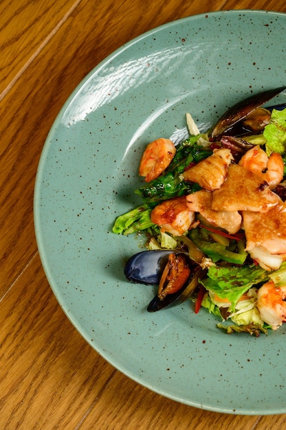 Salad with oysters, shrimps and vegetables on blue plate on wooden background,top view