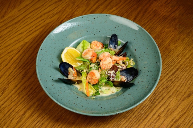 Salad with oysters, shrimps and vegetables on blue plate on wooden background,top view