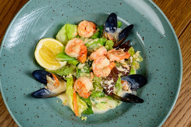 Salad with oysters, shrimps and vegetables on blue plate on wooden background,top view