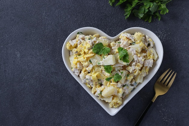 Salad with pineapple baked chicken and omelette in heart shaped plate on a dark gray background