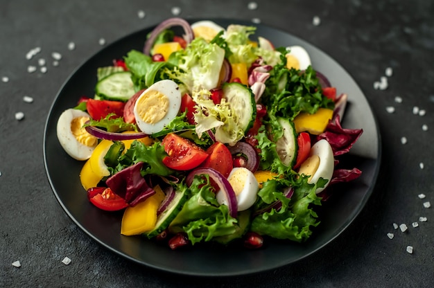 Salad with pomegranate, tomatoes, fresh cucumbers, onions, sesame seeds and cashew nuts, spices on a stone background. Healthy vegetarian food.