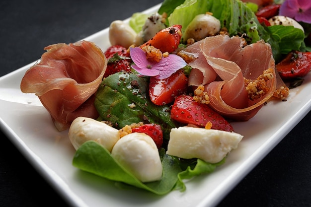 Salad with prosciutto strawberries and mozzarella on a dark