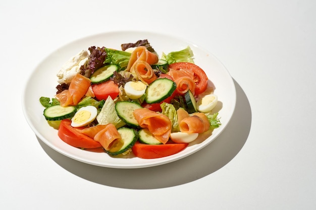 Salad with salmon cucumber tomatoes and cream cheese on a white plate on a white background