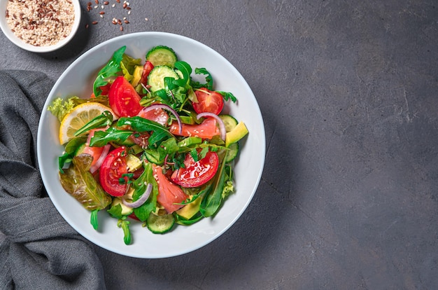 Salad with salmon vegetables and fresh herbs on a dark background