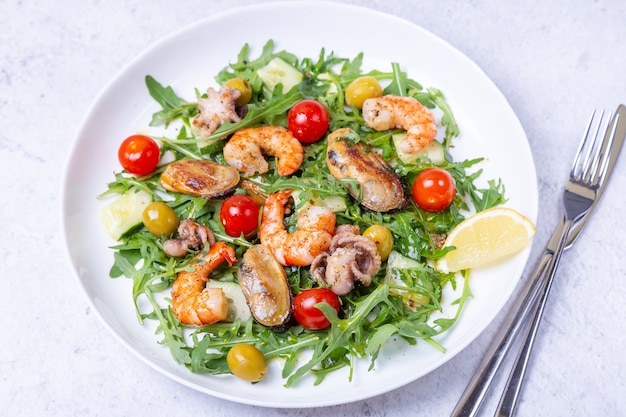 Salad with seafood, arugula, tomatoes, cucumbers and olives on a white plate