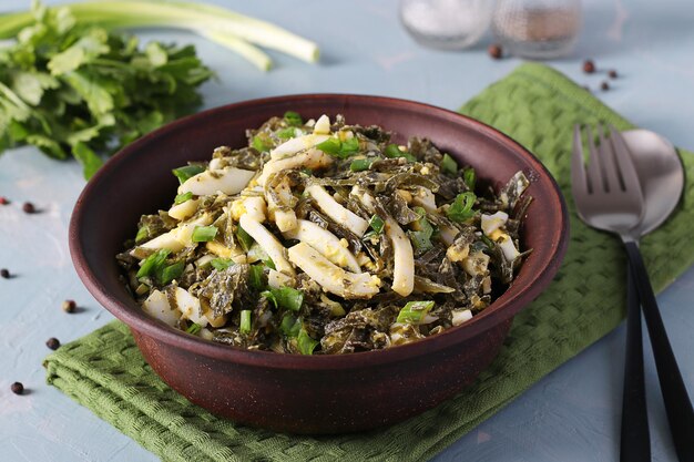 Salad with seaweed squid and green onions in brown bowl on light blue background Closeup