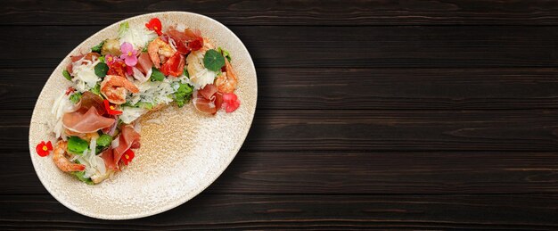 Salad with shrimp prosciutto and cheese on a plate on a wooden background