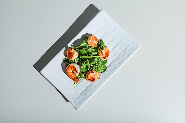 Salad with shrimps and arugula on white dish on white background