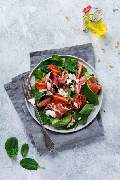 Salad with spinach, cherry tomato, mozzarella, pine nuts and ham with olive oil on an old concrete gray background.