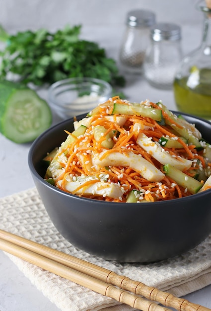 Salad with squid carrots and cucumber sprinkled with sesame seeds in a dark bowl on light background