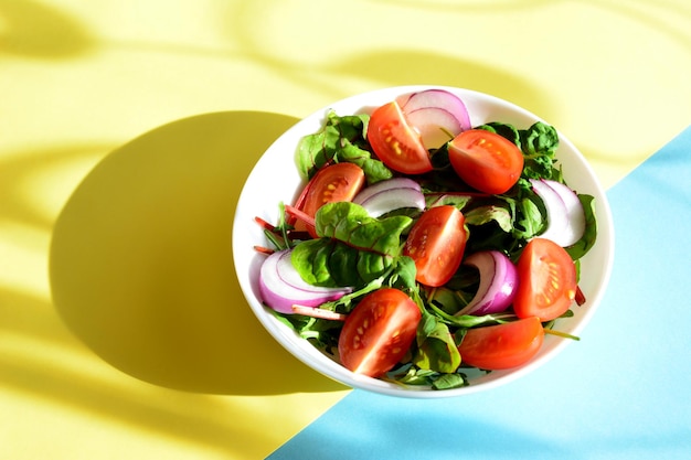 salad with tomato slices, onion and salad greens in white bowl on the yellow and blue background