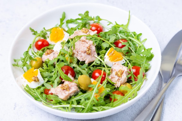 Salad with tuna arugula tomatoes olives and eggs in a white plate A traditional dish Closeup