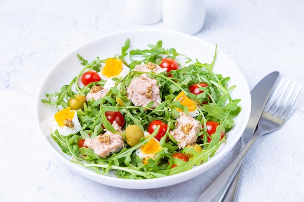 Salad with tuna arugula tomatoes olives and eggs in a white plate A traditional dish Closeup