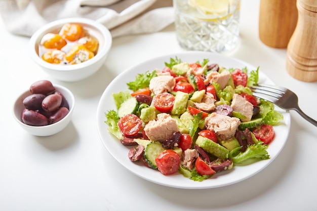 Salad with tuna lettuce cucumbers tomatoes olives and avocados in white plate on the table