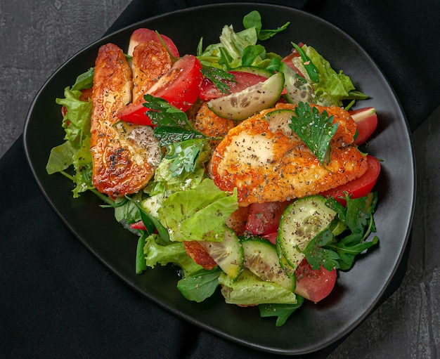 Salad with vegetables and fried halumi cheese with spices. On a black plate. View from above. Dark background backdrop.