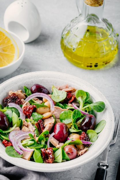 Salad with white beans tuna olives red onions and dried tomatoes with green lettuce leaves in a bowl