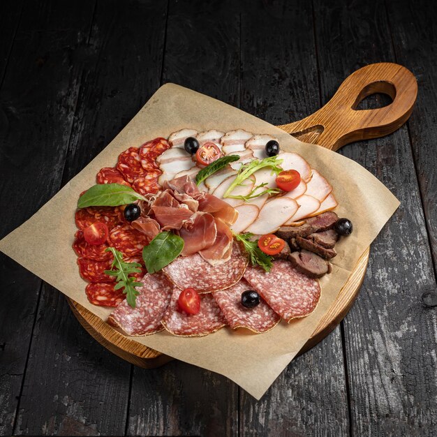 salami with sausage, ham, tomatoes, olives and basil on wooden board