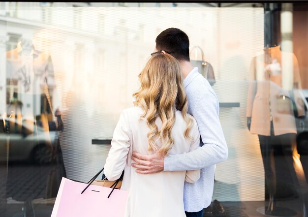 Photo sale, consumerism and people concept - close up of happy couple with shopping bags looking at shop window in city