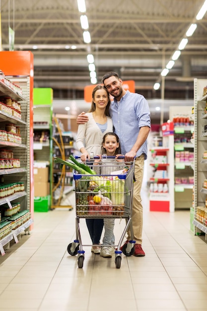 sale, consumerism and people concept - happy family with child and shopping cart buying food at grocery store or supermarket