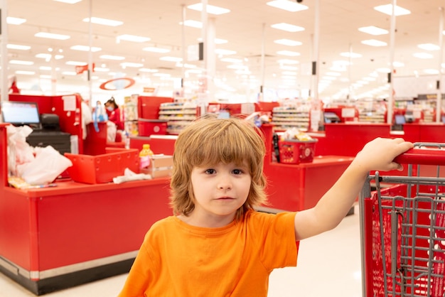 Sale consumerism and people concept  happy little boy with food in shopping cart at grocery store