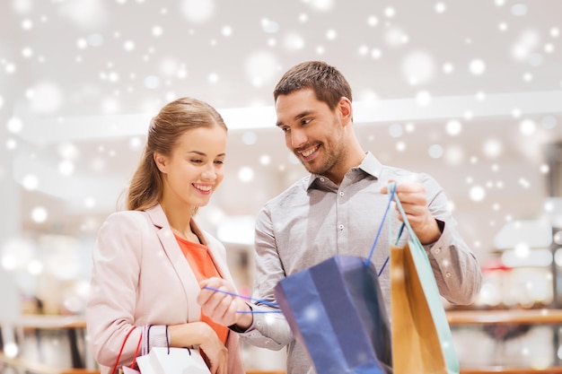 sale, consumerism and people concept - happy young couple showing content of shopping bag in mall with snow effect