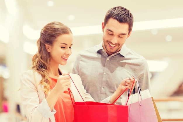 sale, consumerism and people concept - happy young couple showing content of shopping bags in mall