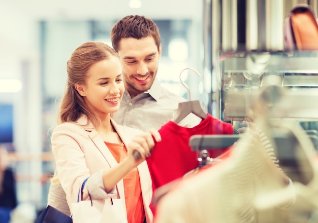 sale, consumerism and people concept - happy young couple with shopping bags choosing dress in mall