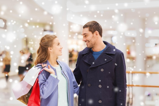 sale, consumerism and people concept - happy young couple with shopping bags talking in mall with snow effect