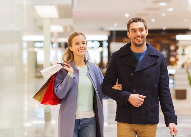 sale, consumerism and people concept - happy young couple with shopping bags walking in mall