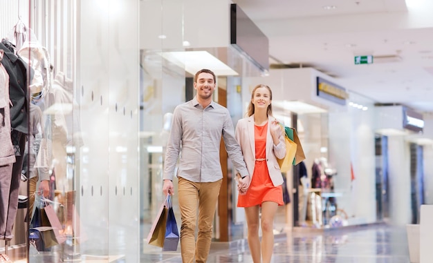 sale, consumerism and people concept - happy young couple with shopping bags walking in mall