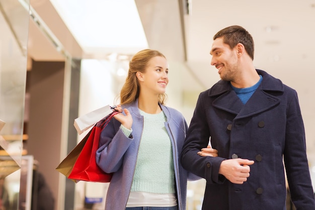 sale, consumerism and people concept - happy young couple with shopping bags walking and talking in mall