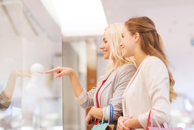 sale, consumerism and people concept - happy young women with shopping bags pointing finger in mall