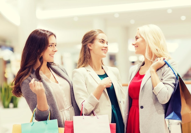 sale, consumerism and people concept - happy young women with shopping bags talking in mall