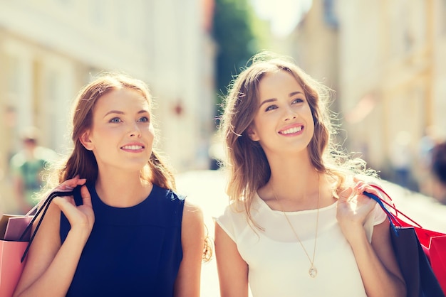 sale, consumerism and people concept - happy young women with shopping bags walking along city street