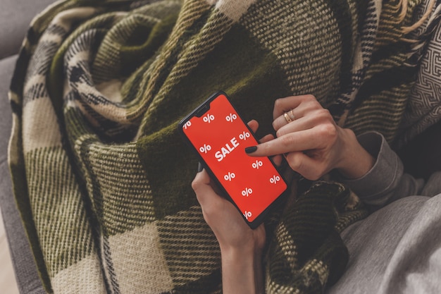 Sale on the phone screen. Woman holds a phone in his hand and sees the inscription sale. Online shopping without leaving home during quarantine. Black friday sale