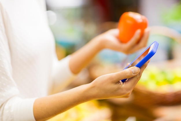 sale, shopping, consumerism and people concept - close up of young woman hands with smartphone and persimmon in market