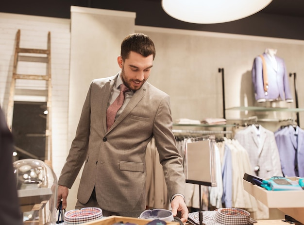 sale, shopping, fashion, style and people concept - happy elegant young man or businessman in suit choosing shirt in mall or clothing store