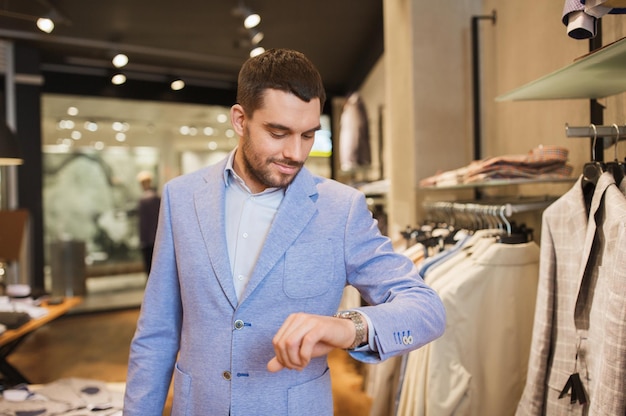 sale, shopping, fashion, style and people concept - happy young man in jacket looking at wristwatch at clothing store