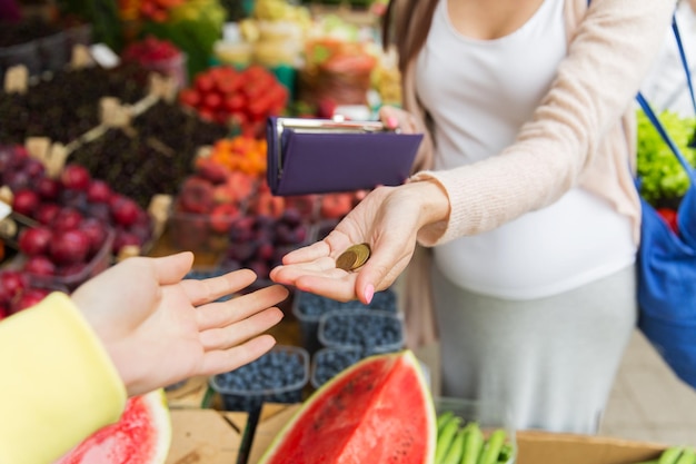 sale, shopping, pregnancy and people concept - close up of pregnant woman with wallet and money buying food at street market