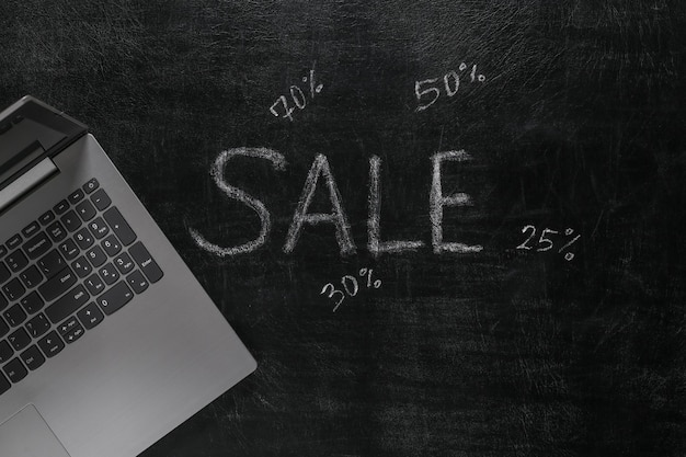 Sale word chalk hand drawn on blackboard with laptop. Shop online. seasonal discounts concept