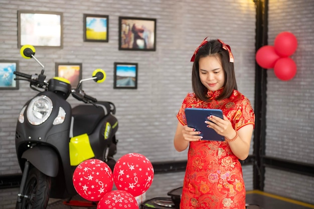 Salesman holding mobile tablet working at motorcycle dealer in showroom Salesmen dressed in traditional Chinese cheongsams for Chinese New Year