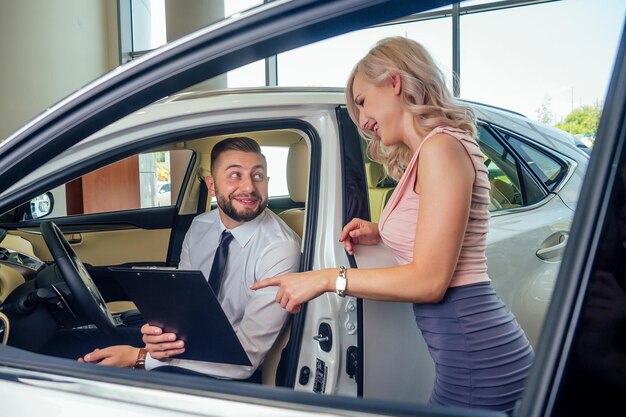 Photo salesman in suit showing catalog to female blonde customer in dealership salon