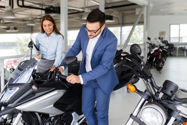 Saleswoman at the dealership showroom talking with customer and helping him to choose a new motorcycle for himself.