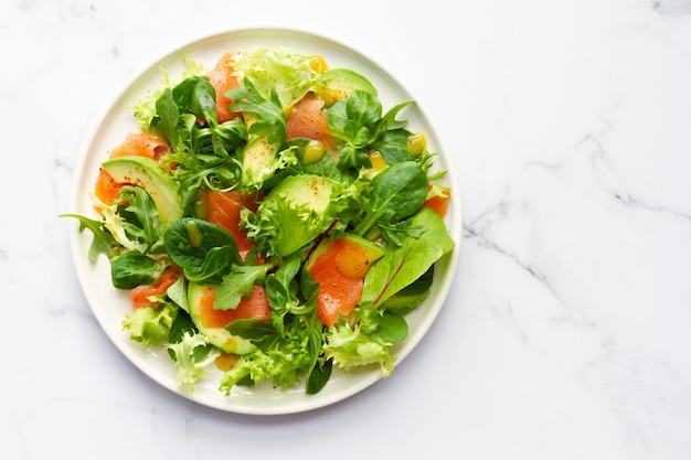 Salmon avocado and assorted lettuce salad on white marble background