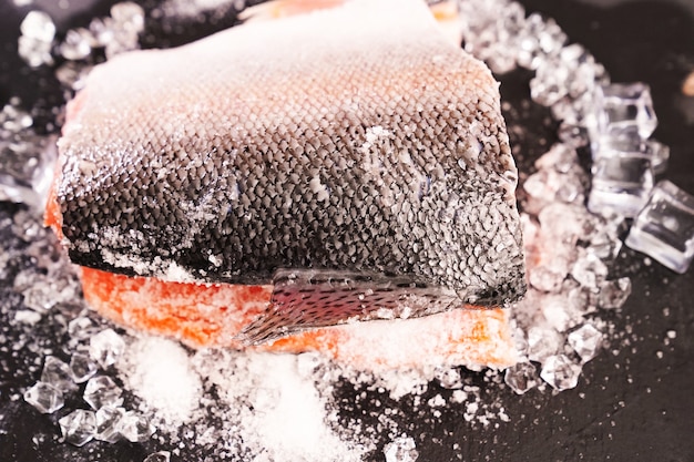 Salmon on a black stone board with ice cubes.