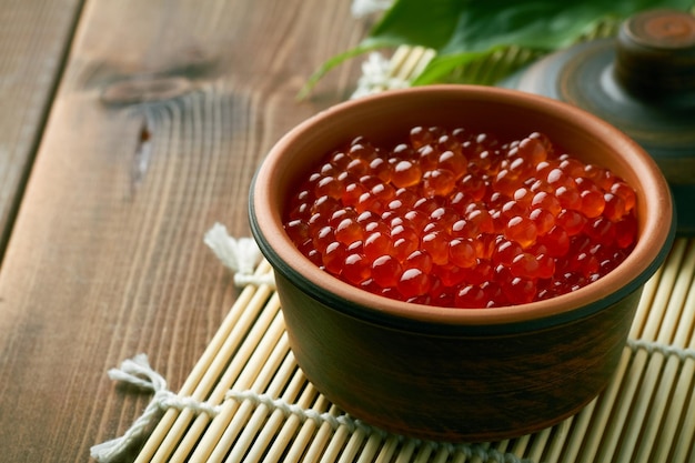 Salmon caviar in a bowl on brown background