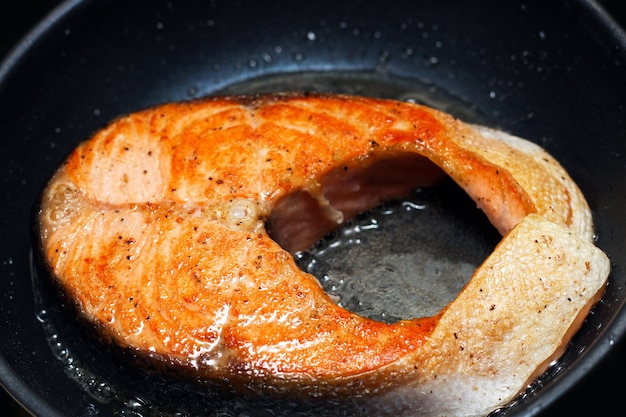 Salmon is fried in a black non-stick skillet. Cooking red fish.